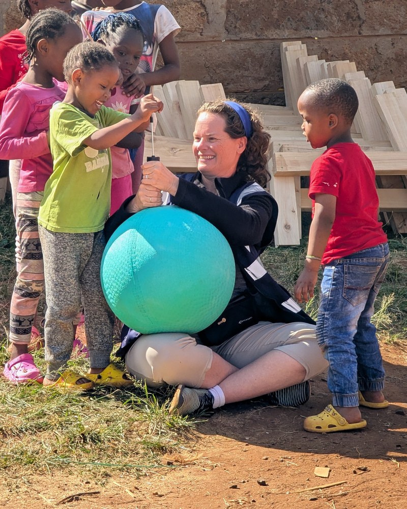 Mindy Hanson kneeling with children and a ball at a TCOLF project in Kenya